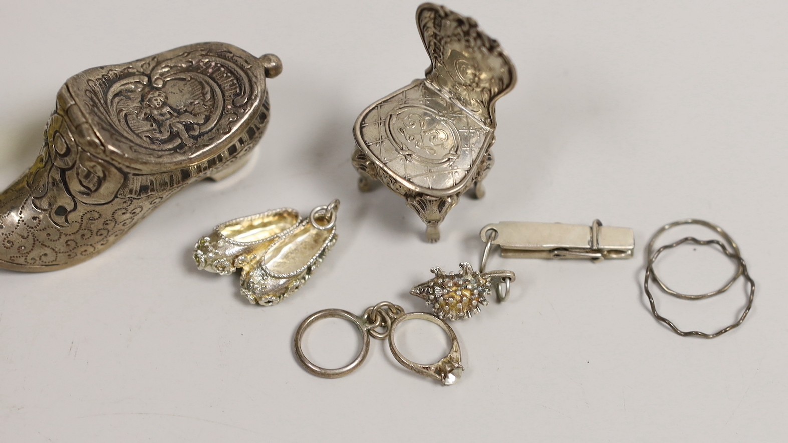 An Edwardian silver miniature model of an occasional chair, import marks for London, 1902, 43mm, a continental white metal model of a shoe and a similar model of a young child, a base metal 'book' box containing a rosary